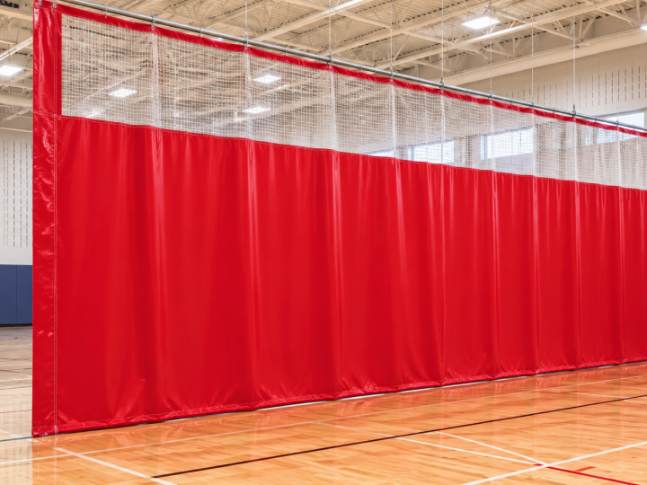 Red vinyl gym divider curtain with a mesh upper section, installed in a gymnasium.